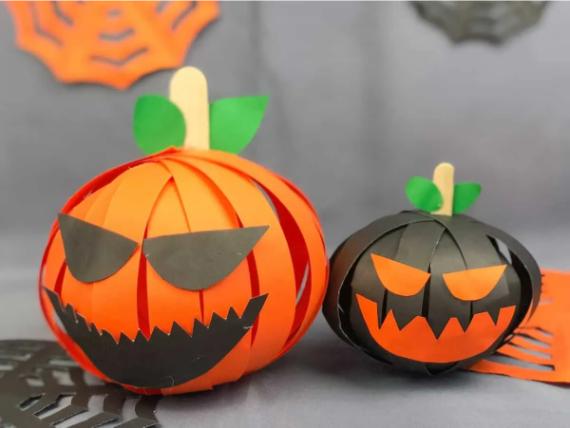 Two paper pumpkins with black and orange facial features, resembling jack-o'-lanterns. They have green leaves and create a playful Halloween vibe.