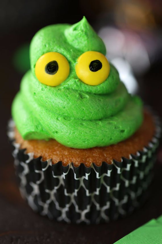 A cupcake with vibrant green frosting shaped like a swirl and topped with two yellow and black eyes, resembling a quirky monster, with a patterned wrapper.