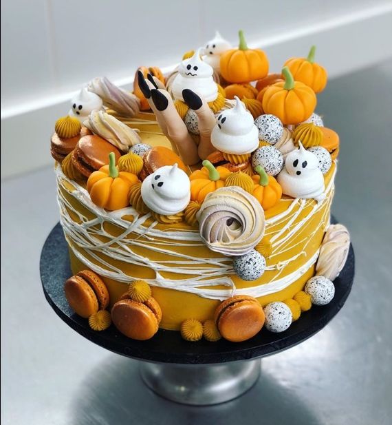 Festive Halloween cake with orange frosting, topped with mini pumpkins, ghosts, colorful meringues, macarons, and playful legs. Spooky and fun.