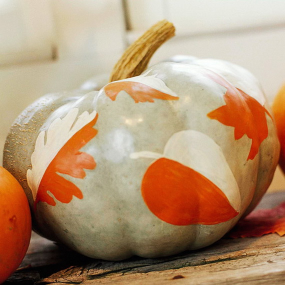 A pale pumpkin painted with orange and white autumn leaves sits on a wooden surface, surrounded by warm, rustic tones, conveying a cozy fall atmosphere.