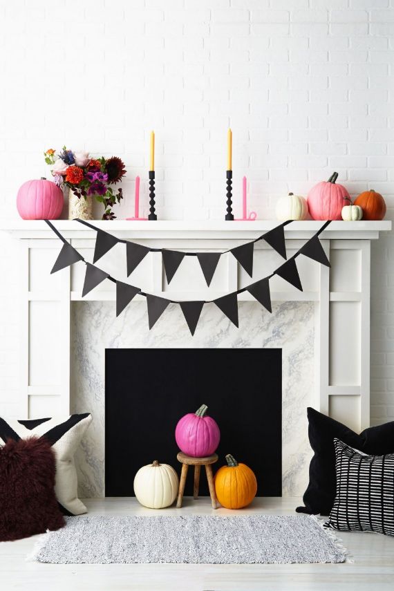 Fireplace decorated for Halloween with pink, white, and orange pumpkins on and below the mantel. Black pennant banner and colorful flowers add a festive touch.