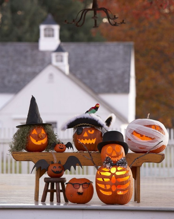 Whimsical Halloween scene with creatively carved pumpkins wearing costumes: witch, pirate, and mummy. A skeleton pumpkin adds charm. Rustic barn in background.